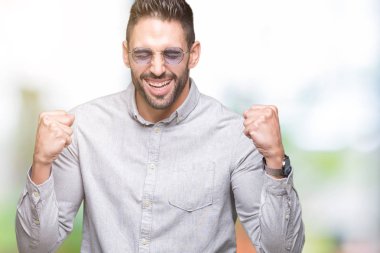 Yakışıklı delikanlı üzerinde güneş gözlüğü takıyor arka plan çok mutlu ve heyecanlı kaldırdı, silah ile kazanan jest yapıyor gülümseyen ve başarı için çığlık izole. Kutlama kavramı.