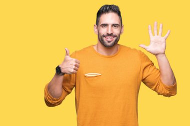 Yakışıklı delikanlı gösterilen ve parmakları ile işaret izole arka plan üzerinde kendinden emin ve mutlu gülümseyerek süre 6 numara.