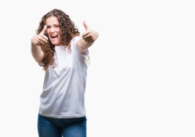 Güzel esmer kıvırcık saçlı Genç kız el ile pozitif jest yapıyor onaylama izole arka plan üzerinde rahat t-shirt giyen başparmak gülümseyen ve başarı için mutlu. Kamera, kazanan jest arıyorsunuz.