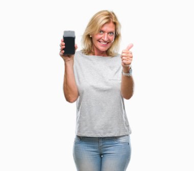 Orta yaş sarışın kadın izole arka plan üzerinde ekranla akıllı telefon ok işareti, başparmak ile parmak, mükemmel işareti yapıyor kocaman bir gülümseme ile mutlu gösterilen