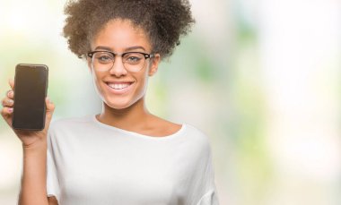 Genç güzel afro Amerikan gösteren smartphone ekran üzerinde duran ve diş gösterilen kendine güvenen bir gülümsemeyle gülümseyerek mutlu bir yüz ile izole arka plan
