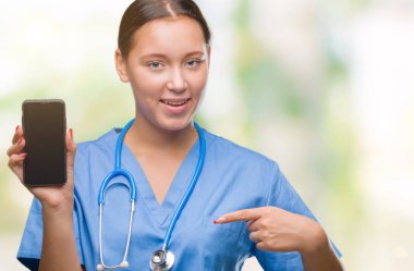 Smarpthone kendisine sürpriz yüz işaret parmağı izole arka plan üzerinde gösterilen Genç beyaz doktor kadın