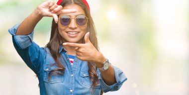 Genç güzel Arap kadın elle yapma çerçeve ve parmakları ile mutlu yüz gülümseyen izole arka plan üzerinde güneş gözlüğü takıyor. Yaratıcılık ve Fotoğrafçılık kavramı.