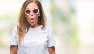 Orta yaş İspanyol kadın korkuyor ve şok sürpriz ifade, korku ve heyecan yüz ile izole arka plan üzerinde moda güneş gözlüğü takıyor.