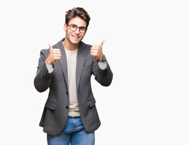 El ile pozitif jest yapıyor izole arka plan başarı işareti üzerinde gözlük takan genç iş adamı başparmak gülümseyen ve mutlu. Neşeli bir ifadeyle, kazanan jest kameraya bakıyor.