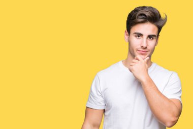 Emin çapraz kollar ve çeneme kaldırdı el ile gülümseme ile kameraya bakarak izole arka plan üzerinde beyaz t-shirt giyen genç yakışıklı adam. Pozitif düşünce.