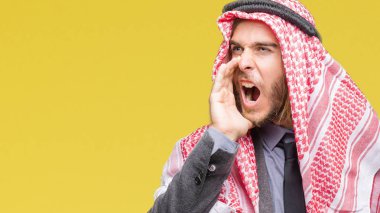 Genç yakışıklı Arap adam uzun saçlı bağırarak ve ağzı üzerinde el ile yan için çığlık izole arka plan üzerinde keffiyeh giyiyor. İletişim kavramı.