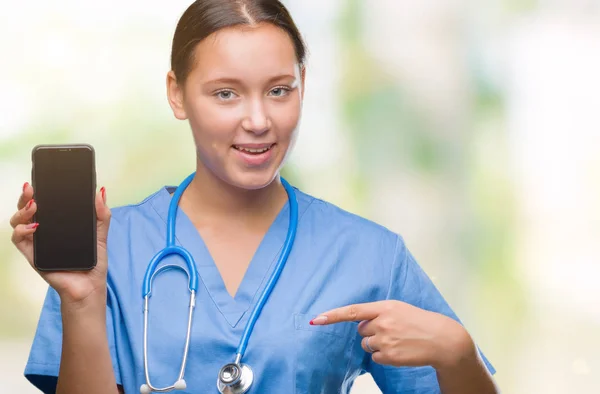 Young caucasian doctor woman showing smarpthone over isolated background with surprise face pointing finger to himself