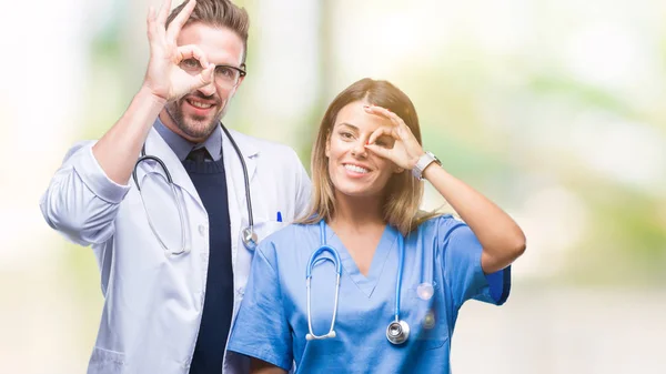 年轻夫妇的医生和外科医生在孤立的背景做确定的手势与手微笑 眼睛通过手指看着快乐的脸 — 图库照片