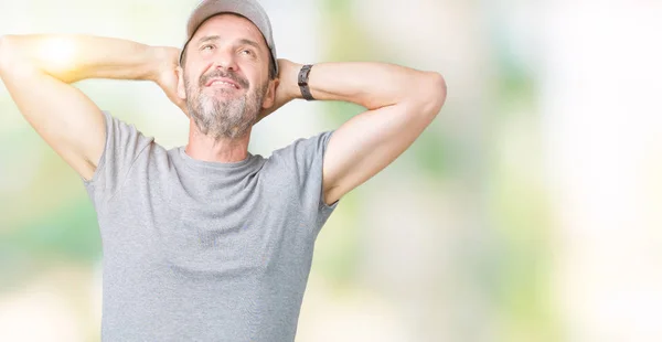 Handsome middle age hoary senior man wearing sport cap over isolated background Relaxing and stretching with arms and hands behind head and neck, smiling happy