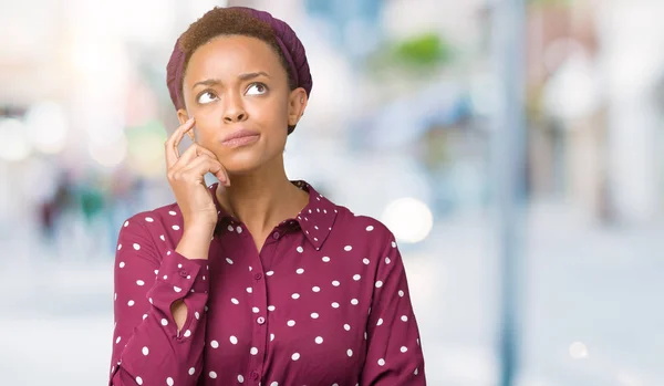 Beautiful young african american woman wearing head scarf over isolated background with hand on chin thinking about question, pensive expression. Smiling with thoughtful face. Doubt concept.