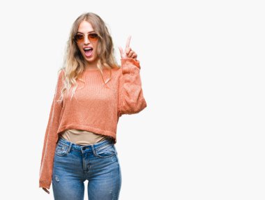 Başarılı fikirle izole arka plan işaret parmağı üzerinde güneş gözlüğü takıyor güzel sarışın genç kadın. Çıktıktan ve mutlu. Bir numara.