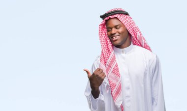 Geleneksel keffiyeh seyir ve başparmak yanında yukarıyı mutlu yüz ile gülümseyen izole arka plan üzerinde giyen genç Arapça Afrika adam.
