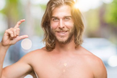 Genç yakışıklı gömleksiz adam uzun saçlı seksi vücut izole arka plan gülümseyen ve süre seyir ve kamera boyutu işaret parmaklarıyla yapıyor el ile kendinden emin eller üzerinde gösterilen. Ölçü kavramı.