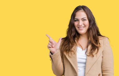 Artı boyutu genç kadın güzel üzerinde kış palto giyiyor arka plan kameraya bakarak yan el ve parmak ile işaret yüzünde kocaman bir gülümseme ile izole.