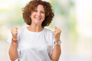 Üzerinde izole arka plan kutluyor t-shirt şaşırttı ve silah ile başarı için hayran beyaz giyen güzel orta ager üst düzey kadın kaldırdı ve gözleri açık. Kazanan kavramı.