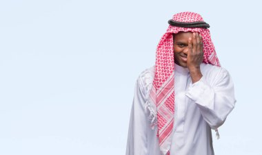 El yüz ve sürpriz duygu kendinden emin gülümseme ile tek gözüyle kapsayan izole arka plan üzerinde geleneksel keffiyeh giyen genç Arapça Afrika adam.
