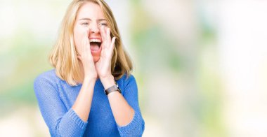 Kızgın ile yüksek sesle bağırarak izole arka plan üzerinde mavi kazak giyen güzel genç kadın ağzına eller