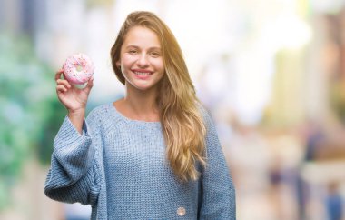 Tatlı çörek yeme izole arka plan üzerinde duran ve diş gösterilen kendine güvenen bir gülümsemeyle gülümseyerek mutlu bir yüz ile genç güzel sarışın kadın