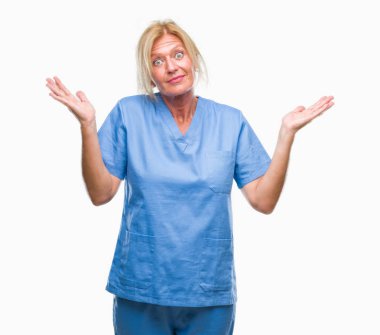 Orta yaş sarışın kadın doktor hemşire üniforması üzerinde arka plan clueless ve şaşkın bir ifadeyle kollar ve eller kaldırdı izole. Şüphe kavramı.