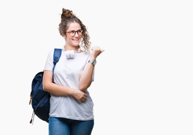 Sırt çantası ve kulaklıklar arıyorsunuz ve başparmak yanında yukarıyı mutlu yüz ile gülümseyen izole arka plan üzerinde giyen genç esmer öğrenci kız.