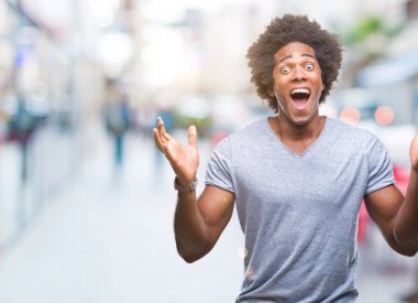 Afro Amerikalı adam deli kutluyor ve silah ile başarı için heyecanlı çığlık kaldırdı ve açık gözleri hayret izole arka plan üzerinde. Kazanan kavramı