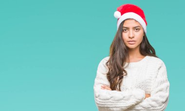 İzole arka plan şüpheci ve sinir, onaylamayan ifade yüz çapraz kolları üzerinde Noel şapka giyen genç Arap kadın. Negatif kişi.