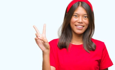 Genç Asyalı kadın mutlu yüz zafer işareti yaparken kameraya göz kırpıyor ile gülümseyen izole arka plan üzerinde. İki numaralı.