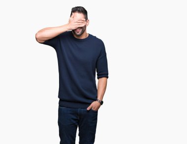 Genç yakışıklı adam gülümsüyor ve gözleri için sürpriz kapsayan yüz el ile gülüyor izole arka plan üzerinde kazak giyiyor. Kör kavramı.