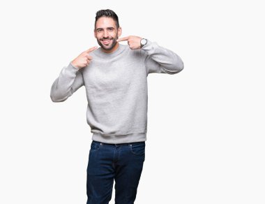 Genç yakışıklı adam kendinden emin gösterilen ve işaret parmakları diş ve ağız ile gülümseyen izole arka plan üzerinde kazak giyiyor. Sağlık kavramı.