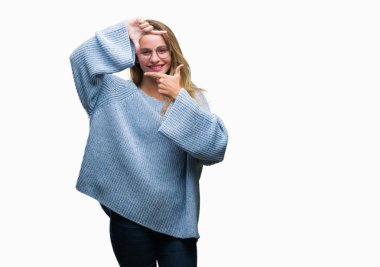 Kazak ve gözlük elle yapma çerçeve ve parmakları ile mutlu yüz gülümseyen izole arka plan üzerinde giyen genç güzel sarışın kadın. Yaratıcılık ve Fotoğrafçılık kavramı.