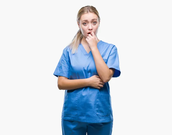 若い金髪の外科医医師女性は不安や両手の爪を噛んで口の中で緊張を探して孤立の背景に医療制服を着てします 不安の問題 — ストック写真