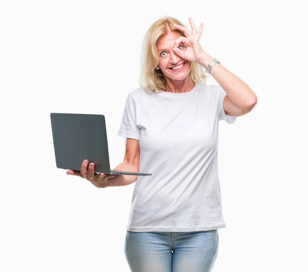 中年金发碧眼的女人使用电脑笔记本电脑在孤立的背景与快乐的脸微笑做确定的标志与眼睛看着手指 — 图库照片