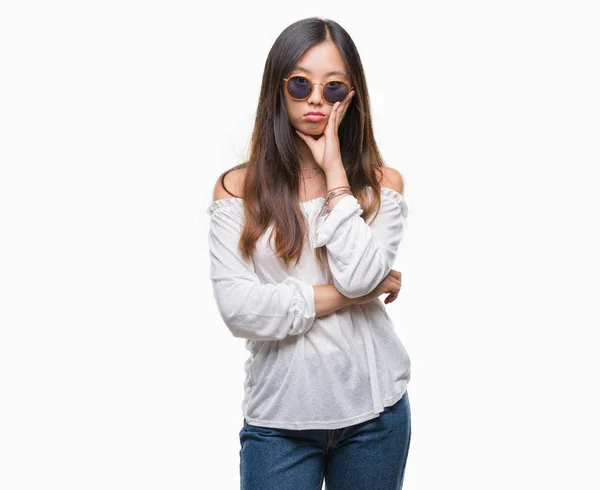 年轻的亚洲妇女戴着太阳镜在孤立的背景下思考疲倦和厌倦与交叉手臂的抑郁症问题 — 图库照片