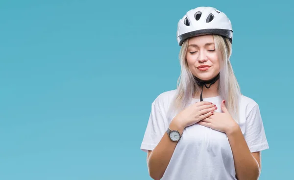 年轻的金发女子戴着骑自行车的安全头盔在孤立的背景微笑与手在胸部与紧闭的眼睛和感恩的手势在脸上 健康理念 — 图库照片