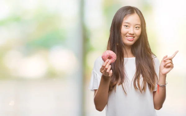 Молодая Азиатская Женщина Ест Пончики Изолированном Фоне Счастливо Указывая Рукой — стоковое фото