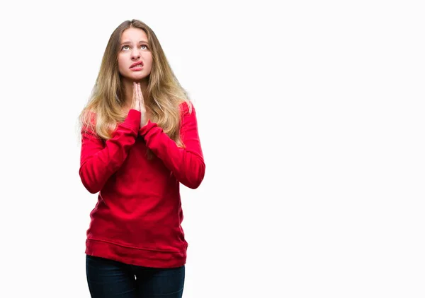 Young beautiful blonde woman wearing red sweater over isolated background begging and praying with hands together with hope expression on face very emotional and worried. Asking for forgiveness. Religion concept.