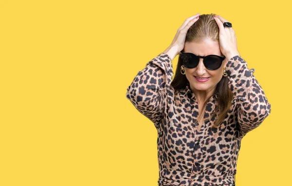 Middle age mature rich woman wearing sunglasses and leopard dress over isolated background suffering from headache desperate and stressed because pain and migraine. Hands on head.