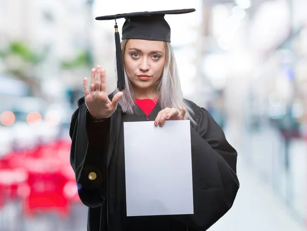 防衛ジェスチャー 深刻な自信を持って式に一時停止の標識を行うオープンの手で隔離された背景の上の学位を保持する大学院の制服を着て若いブロンドの女性 — ストック写真