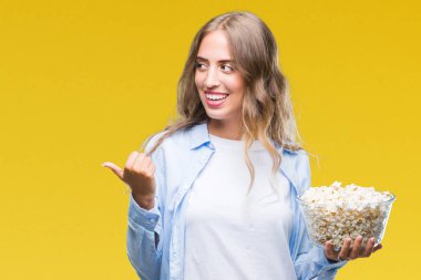 İşaret ve başparmak kadar mutlu yüz gülümseyen tarafı ile gösteren izole arka plan üzerinde patlamış mısır yemek güzel sarışın genç kadın