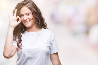 Güzel esmer kıvırcık saçlı Genç kız üzerinde gülümseyen izole arka plan el ve parmaklar ok işaretiyle yapıyor olumlu rahat t-shirt giyiyor. Başarılı ifade.
