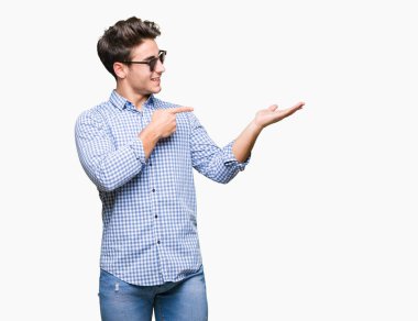 Yakışıklı delikanlı hayrete ve el ile sunulması ve parmak ile işaret ederken kameraya gülümseyen izole arka plan üzerinde güneş gözlüğü takıyor.