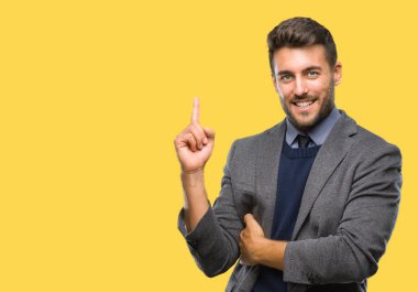 Kameraya bakarak yan el ve parmak ile işaret eden genç yakışıklı iş adamı yüzünde kocaman bir gülümseme ile izole arka plan üzerinde.