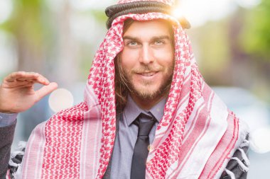 Genç yakışıklı Arap adam uzun saçlı ile büyük ve büyük boy işaret, ölçü birimi sembol gösteren el eller izole arka plan üzerinde keffiyeh giyiyor. Kameraya bakarak gülümsüyordu. Ölçüm kavramı.