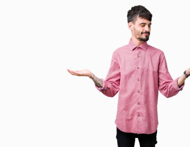Gülen iki elle gösterilen açık avuç içi, sunma ve karşılaştırma ve denge reklam arka plan üzerinde pembe gömlek giymiş genç yakışıklı adam izole
