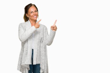 Gülümseyen ve iki elleri ve parmakları ile tarafına işaret kamera bakarak izole arka plan üzerinde kış kazak giyen güzel orta yaş yetişkin kadın.