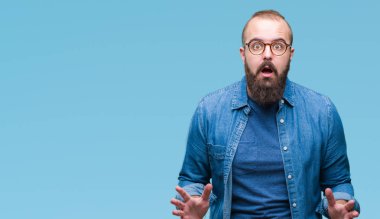 Üzerinde gözlük takan Genç beyaz hipster adam arka plan korkuyor ve şok sürpriz ifade, korku ve heyecan yüz ile izole.