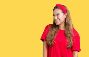 Uzak tarafına yüzünde, doğal ifade gülümseme ile seyir izole arka plan üzerinde kırmızı t-shirt giyen genç güzel esmer kadın. Kendine güvenen gülüyor.