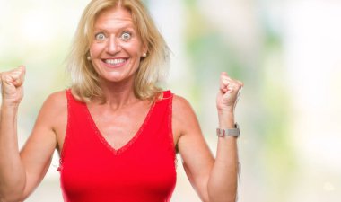 Orta yaş sarışın kadın kutluyor izole arka plan üzerinde şaşırttı ve başarı için kaldırdı kollarını açarak hayret ve gözleri açık. Kazanan kavramı.