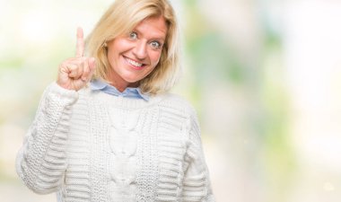 Orta yaş sarışın kadın başarılı fikirle izole arka plan işaret parmağı üzerinde kış kazak giyiyor. Çıktıktan ve mutlu. Bir numara.